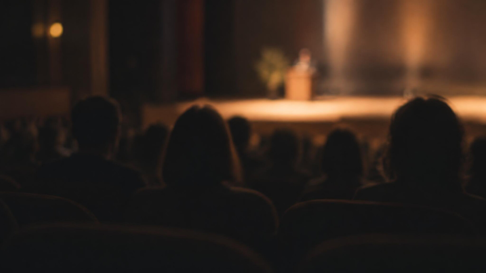 Blurred silhouettes of an audience in dim theatre light